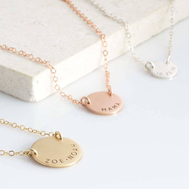 May include: Three gold necklaces with round pendants. The pendants are engraved with the words "MAMA", "ZOE.NOAH", and "10.23.10".