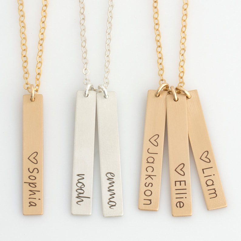 May include: Three gold bar necklaces with personalized names. The first necklace has the name "Sophia" engraved on it. The second necklace has the names "Emma" and "Noah" engraved on it. The third necklace has the names "Jackson", "Ellie", and "Liam" engraved on it.