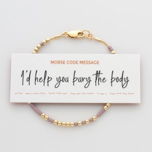 May include: A gold bracelet with a message in Morse code that reads "I'd help you bury the body". The bracelet is made of small gold and purple beads.