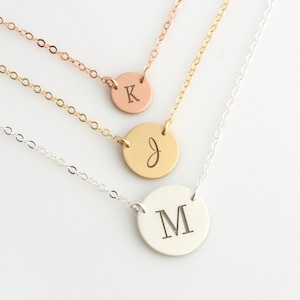 May include: Three gold necklaces with round pendants featuring the letters K, J, and M. The necklaces are layered on a white background.