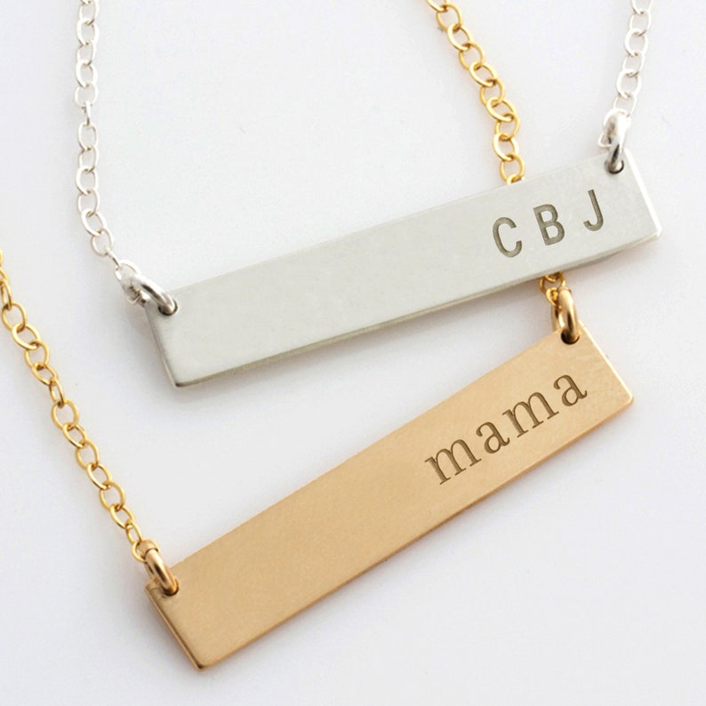 Op de afbeelding: Twee gouden en zilveren bar kettingen met gegraveerde tekst. De zilveren ketting heeft de tekst "CBJ" en de gouden ketting heeft de tekst "mama".