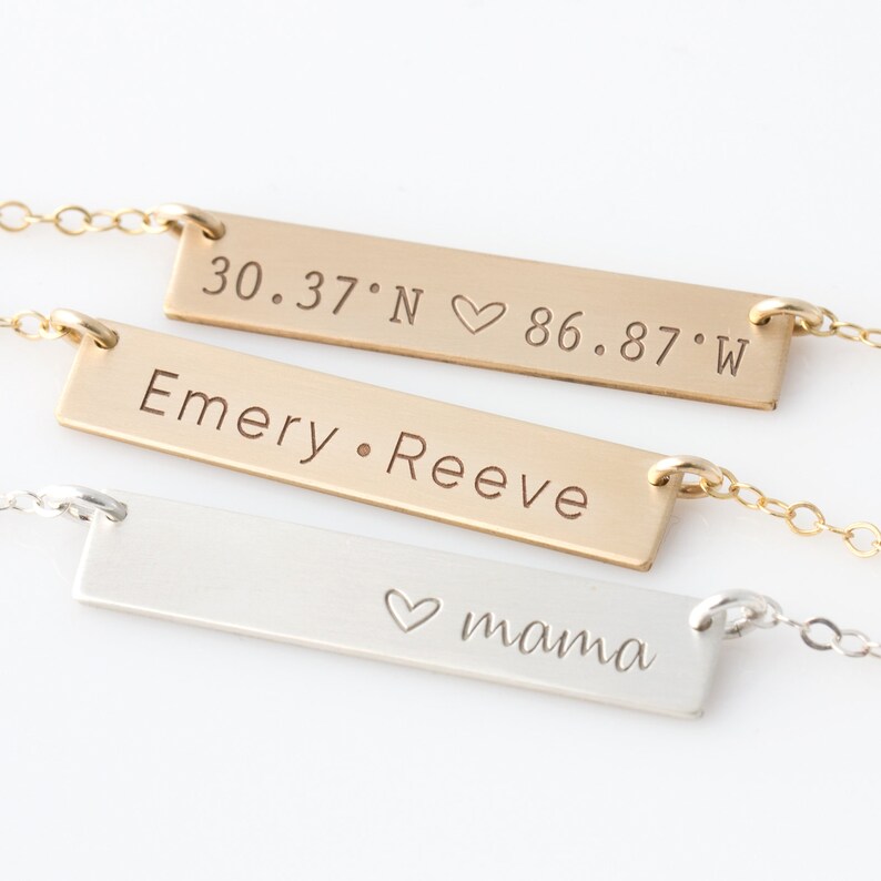 Op de afbeelding: Drie gouden bar kettingen met verschillende inscripties. De bovenste ketting heeft de co&ouml;rdinaten "30.37&deg;N &hearts; 86.87&deg;W". De middelste ketting heeft de inscriptie "Emery. Reeve". De onderste ketting heeft de inscriptie "&hearts; mama".