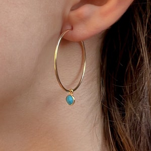 May include: Gold hoop earrings with a turquoise stone charm hanging from the bottom.