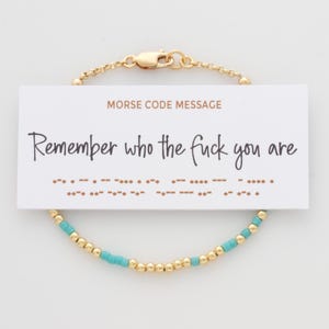 May include: A gold-colored chain bracelet with turquoise beads and a card that reads "Remember who the fuck you are" in cursive. The card also has a Morse code message. The bracelet has a lobster clasp.