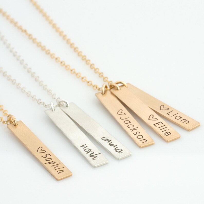May include: Four gold and silver necklaces with personalized bar pendants. The pendants are engraved with the names "Sophia", "Noah", "Emma", "Jackson", "Ellie", and "Liam".