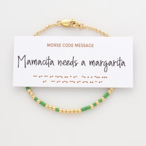 May include: A gold chain bracelet with green beads and a card that reads "Mamacita needs a margarita" in Morse code.
