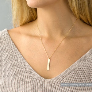 May include: A gold necklace with a vertical bar pendant engraved with the text "07.10.2015". The model is wearing an 18-inch chain.
