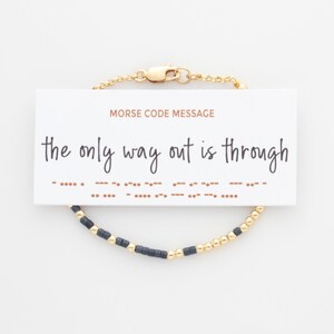May include: A gold chain bracelet with black and gold beads. The bracelet has a message in Morse code that reads "the only way out is through".