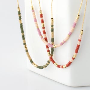 May include: Four beaded necklaces with gold-coloured chains and accents. The beads are in shades of green, tan, pink, and red. The necklaces are displayed against a white background.