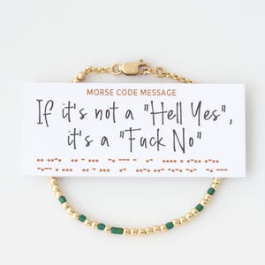 May include: Gold-toned beaded bracelet with a card that reads "If it's not a 'Hell Yes', it's a 'Fuck No'" in black text. The bracelet has green square beads interspersed with the gold beads. The card also has a Morse code message.