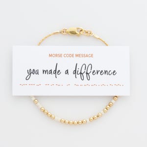 Peut inclure: Bracelet en perles dorées et blanches, avec le message "you made a difference" en code morse.