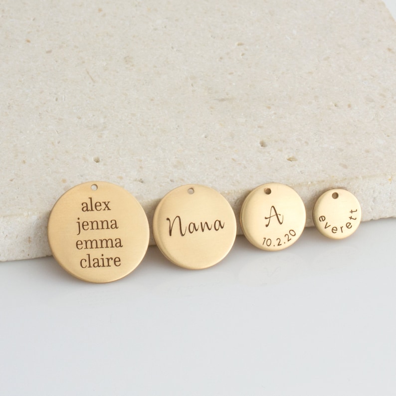 May include: Four gold-colored metal discs with engraved text. The largest disc reads "alex jenna emma claire". The next largest disc reads "Nana". The third disc reads "A 10.2.20". The smallest disc reads "everett".