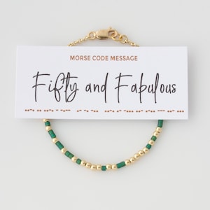 May include: A gold and green beaded bracelet with a card that reads "Morse Code Message Fifty and Fabulous".