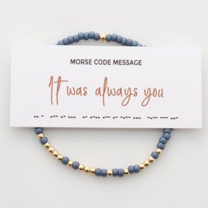 Könnte beinhalten: Ein blaues Perlenarmband mit goldenen Perlen und einer Karte mit der Aufschrift "Morse Code Message It was always you" und der Botschaft in Morsecode darunter.