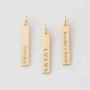 May include: Three gold bar pendants with personalized engravings. The first pendant reads "Gabriela", the second reads "K ♥ E ♥ D", and the third reads "Brooke + Steve".