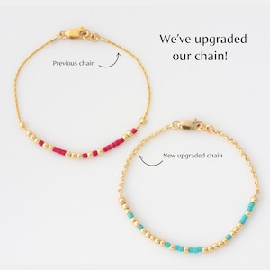 K&ouml;nnte beinhalten: Zwei goldene Armb&auml;nder mit einer Kette und kleinen Perlen. Das obere Armband hat rote Perlen und das untere Armband hat t&uuml;rkisfarbene Perlen. Der Text "We've upgraded our chain!" ist im Bild zu sehen. Das obere Armband ist mit "Previous chain" und das untere Armband mit "New upgraded chain" beschriftet.