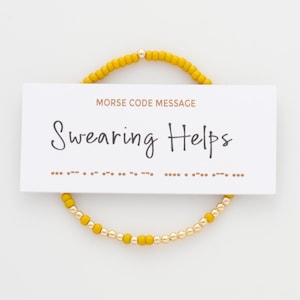 Peut inclure: Un bracelet en perles jaunes avec des perles dorées et une carte qui indique "Message en code Morse : Jurer aide" avec le code Morse du message ci-dessous.
