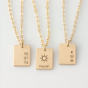 May include: Three gold necklaces with square pendants. The pendants have different engravings: one says "10 01 76", another has a sun and the word "Hazel", and the last one says "K ♥ M".