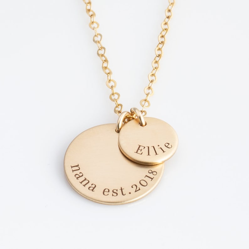 May include: Gold necklace with two round pendants. The larger pendant is engraved with "mama est. 2018" and the smaller pendant is engraved with "Ellie".
