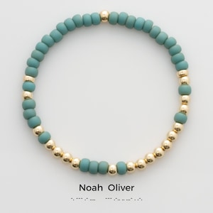 May include: A teal and gold beaded bracelet with the name "Noah Oliver" and braille lettering.