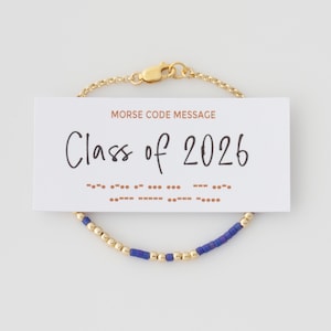 May include: A gold chain bracelet featuring alternating blue and gold beads, displayed with a white card that reads MORSE CODE MESSAGE Class of 2026, accompanied by the corresponding Morse code dots and dashes printed in brown ink.