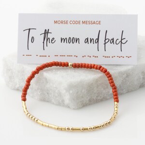 May include: A red and gold beaded bracelet with a card that reads "Morse Code Message" and "To the moon and back".