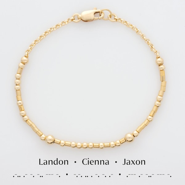 May include: A gold beaded bracelet with a clasp closure. The bracelet has a simple design with alternating round and rectangular beads. The text "Landon. Cienna. Jaxon" is printed below the bracelet.