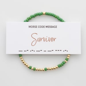 May include: Green and gold beaded bracelet with a card that reads "Morse Code Message" and "Survivor" with the Morse code for the word below.