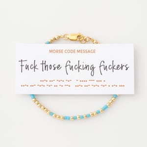 Peut inclure: Un bracelet de perles dorées avec des perles turquoise et un fermoir doré. Une carte blanche avec le texte "MORSE CODE MESSAGE" et "Fuck those fucking fuckers" est attachée au bracelet.