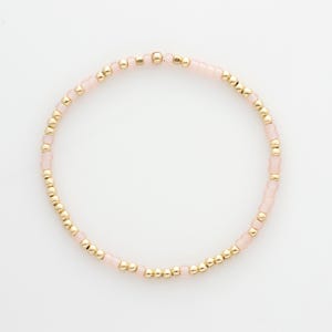 May include: A delicate bracelet with small pink and gold beads. The bracelet is made with a simple design and is perfect for everyday wear.