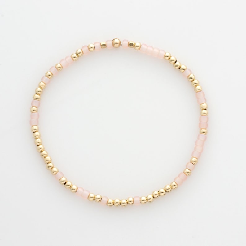 May include: A delicate bracelet with small pink and gold beads. The bracelet is made with a simple design and is perfect for everyday wear.