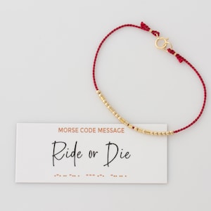 Könnte beinhalten: Rotes Armband mit goldenen Perlen, die die Morse-Code-Botschaft "Ride or Die" buchstabieren.