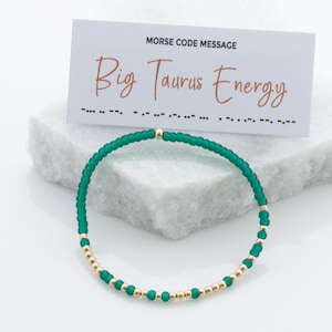 May include: Green and gold beaded bracelet with a card that reads "Big Taurus Energy" in Morse code.