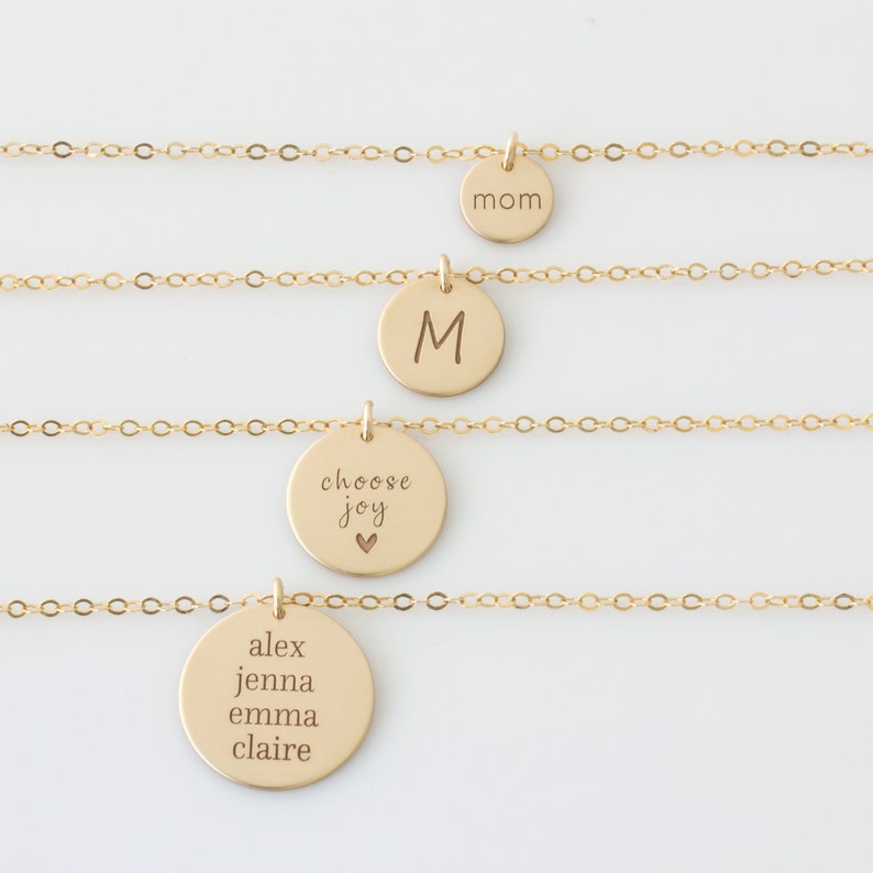 May include: Four gold necklaces with different charms. The top necklace has a charm that says "mom". The second necklace has a charm with the letter "M". The third necklace has a charm that says "choose joy" with a small heart symbol. The bottom necklace has a charm that says "alex jenna emma claire".