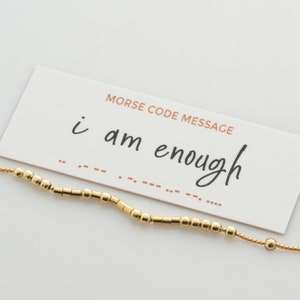 May include: A gold beaded bracelet with a card that reads "Morse Code Message: i am enough". The card shows the Morse code for the message.