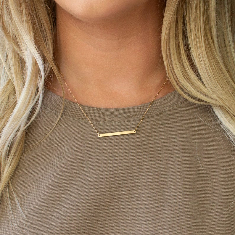 Puede incluir: Un collar de barra de oro con una cadena delicada. El collar es simple y elegante, perfecto para el uso diario.