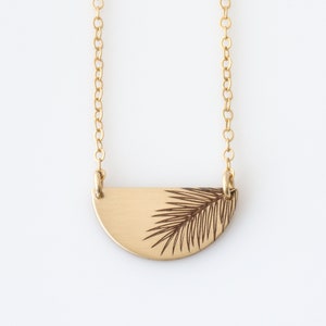May include: A gold necklace with a half-circle pendant featuring a palm leaf design.