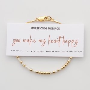 May include: A gold and white beaded bracelet with a card that reads "Morse Code Message: You make my heart happy".