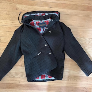 May include: A black quilted jacket with a hood and a red, white, and blue plaid lining. The jacket features a front zipper closure with silver-tone metal snaps, long sleeves, and a Pendleton brand label sewn into the interior neck area.