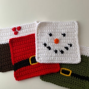 May include: Four crocheted squares, each with a different design. One square is white with a snowman face, one is red with a black belt, one is green with a black belt, and one is brown with red hearts.