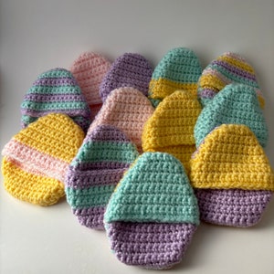 May include: A collection of crocheted Easter eggs in various pastel colors, including yellow, pink, purple, and green. The eggs are striped and solid.