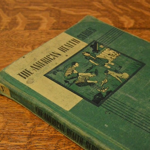 May include: A green book titled "The American Health Series" with the words "Health at Work and Play" and "Wilson Pryor -  Clarence" on the cover.