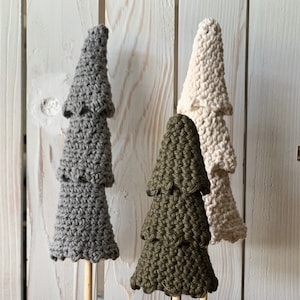 May include: Three crocheted Christmas trees on wooden bases. The trees are grey, green, and white. The bases are made of natural wood and have a rustic look.