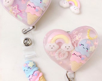 May include: Two pink heart-shaped badge holders with clear resin and glitter. Each holder features a rainbow, clouds, and a stack of ice cream cones with a star on top. One holder has a separate rainbow and cloud charm.