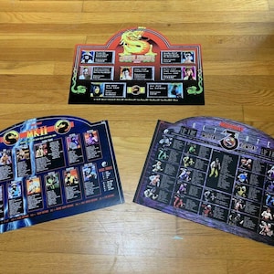 May include: Three Mortal Kombat game posters featuring character lists and images. The posters are in a blue, purple and red colour scheme. The posters are titled "Mortal Kombat II", "Ultimate Mortal Kombat 3" and "Mortal Kombat".