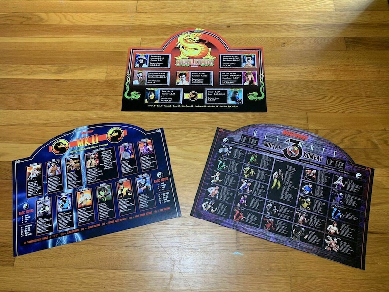 May include: Three Mortal Kombat game posters featuring character lists and images. The posters are in a blue, purple and red colour scheme. The posters are titled "Mortal Kombat II", "Ultimate Mortal Kombat 3" and "Mortal Kombat".