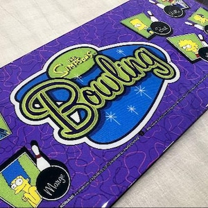 May include: A purple and blue The Simpsons Bowling arcade game control panel with images of Homer, Marge, Bart, Lisa, and other characters. The game title is "The Simpsons Bowling".