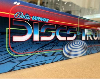 May include: A blue and red pinball machine cabinet with the text "Bally MIDWAY DISCS OF IRON" on the front. The cabinet has a blue and white striped disc on the front.
