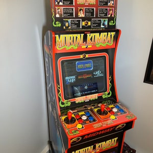 May include: A red and black arcade cabinet with the words "Mortal Kombat 2" on the front. The cabinet has a dragon design on the top and a screen that displays the game's title.