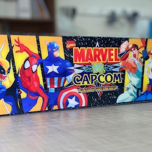 Pode incluir: Painel colorido com personagens de Marvel vs. Capcom. Wolverine, Homem-Aranha e Capitão América à esquerda, Ryu e outros à direita. O título "MARVEL vs. CAPCOM" está em destaque.